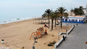A beach with a playground, palm trees, and a paved walkway. - Leonor 3º2ª - Calafell (Calafell)