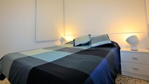 Un dormitorio con una cama, dos mesitas de noche, una mesita blanca y un aplique de pared.