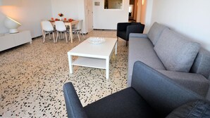 Una sala de estar moderna con un sofá gris, una mesa de centro blanca y un comedor con mesa y sillas.