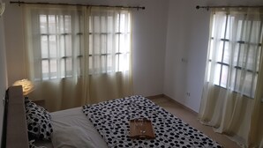 A bedroom with a bed, a bedside table, and curtains. - R&Rhome appartement meublé (Cotonou)