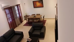 A living room with a sofa set, a dining table with chairs, and a painting on the wall. - R&Rhome appartement meublé (Cotonou)