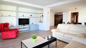 Una sala de estar moderna con un televisor de pantalla plana, sofás rojo y blanco, una mesa de centro y un comedor con una mesa y sillas.