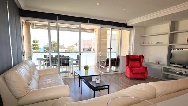 Una sala de estar moderna con un sofá, un sillón rojo, una mesa de centro de vidrio y un televisor.
