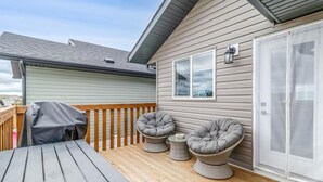 En overdækket terrasse med et bord og to polstrede stole, en skydedør af glas samt et vindue med en lampe.