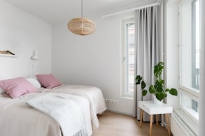 A bedroom with a bed, a bedside table, a hanging light, and a window with curtains.