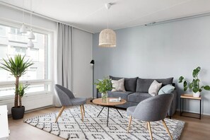 A modern living room with a grey sofa, two armchairs, a coffee table, and a hanging light fixture.