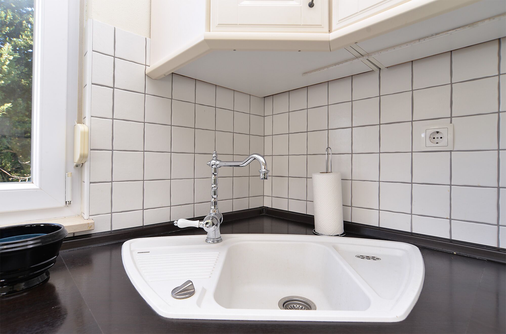 Cucina con lavello bianco, piano di lavoro nero e schienale piastrellato in bianco.