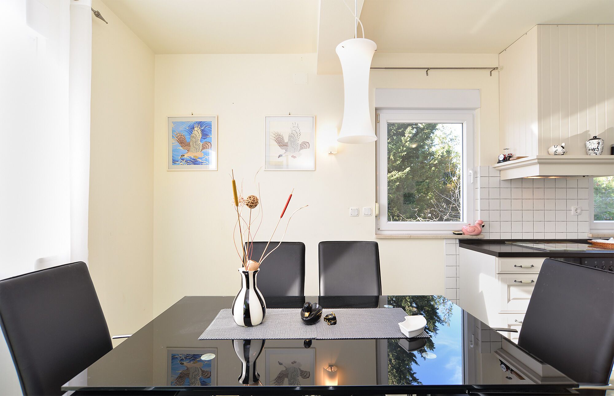 Een moderne eetruimte met een glazen tafel, zwarte stoelen en een vaas met decoratieve takken.
