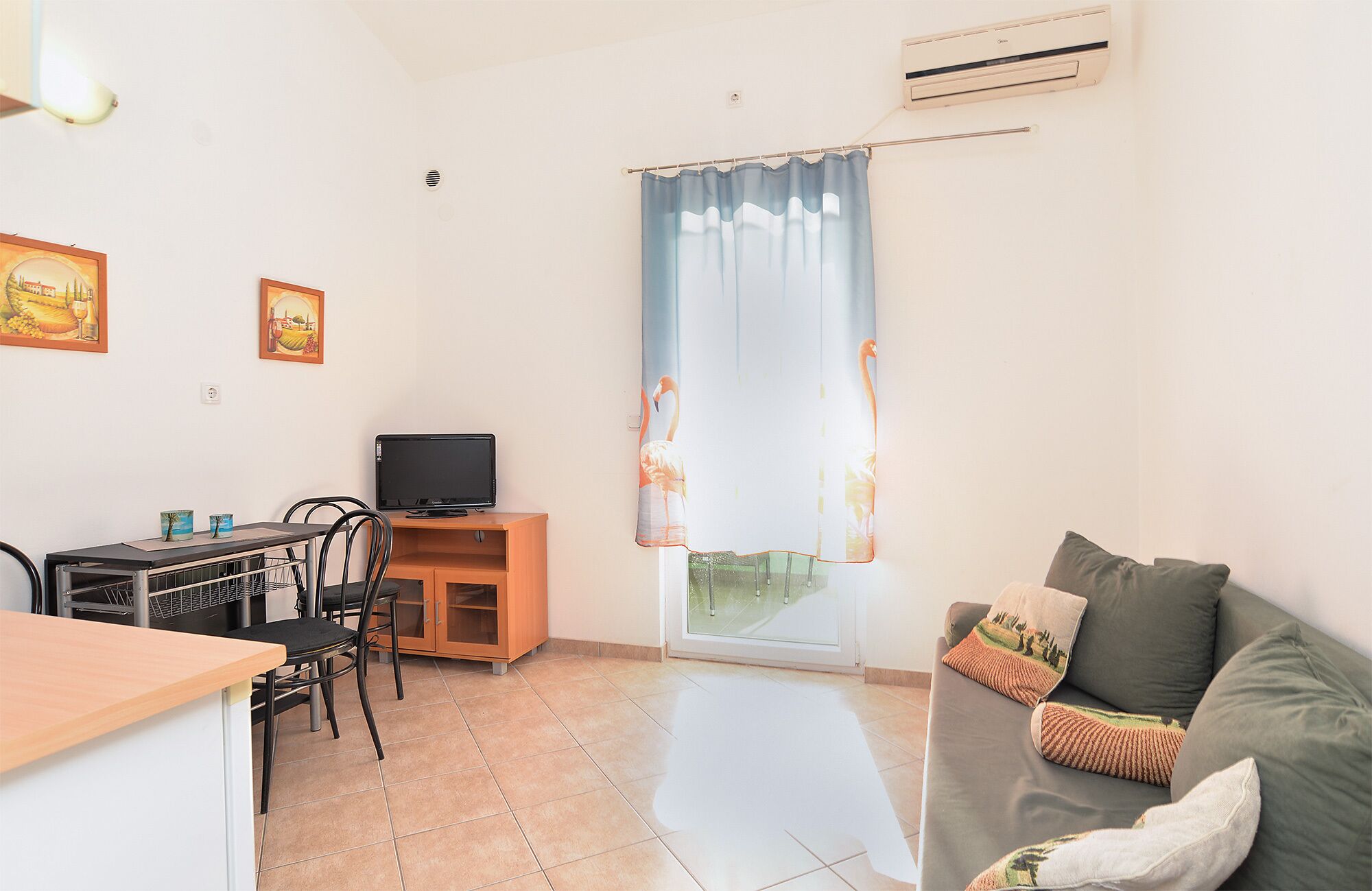 A compact living space with a kitchenette, a dining area, a sofa with decorative pillows, and a large window with curtains.