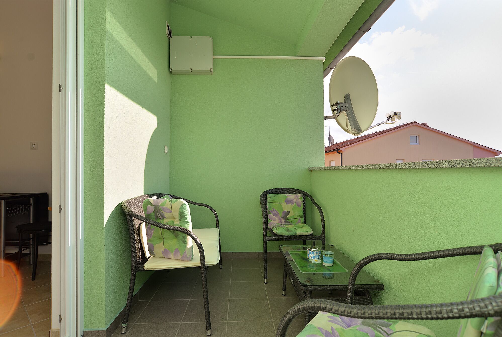 A balcony with two wicker chairs, a small table, and a satellite dish.