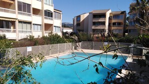 Une piscine entourée d’une clôture blanche, avec un immeuble à plusieurs étages en arrière-plan.