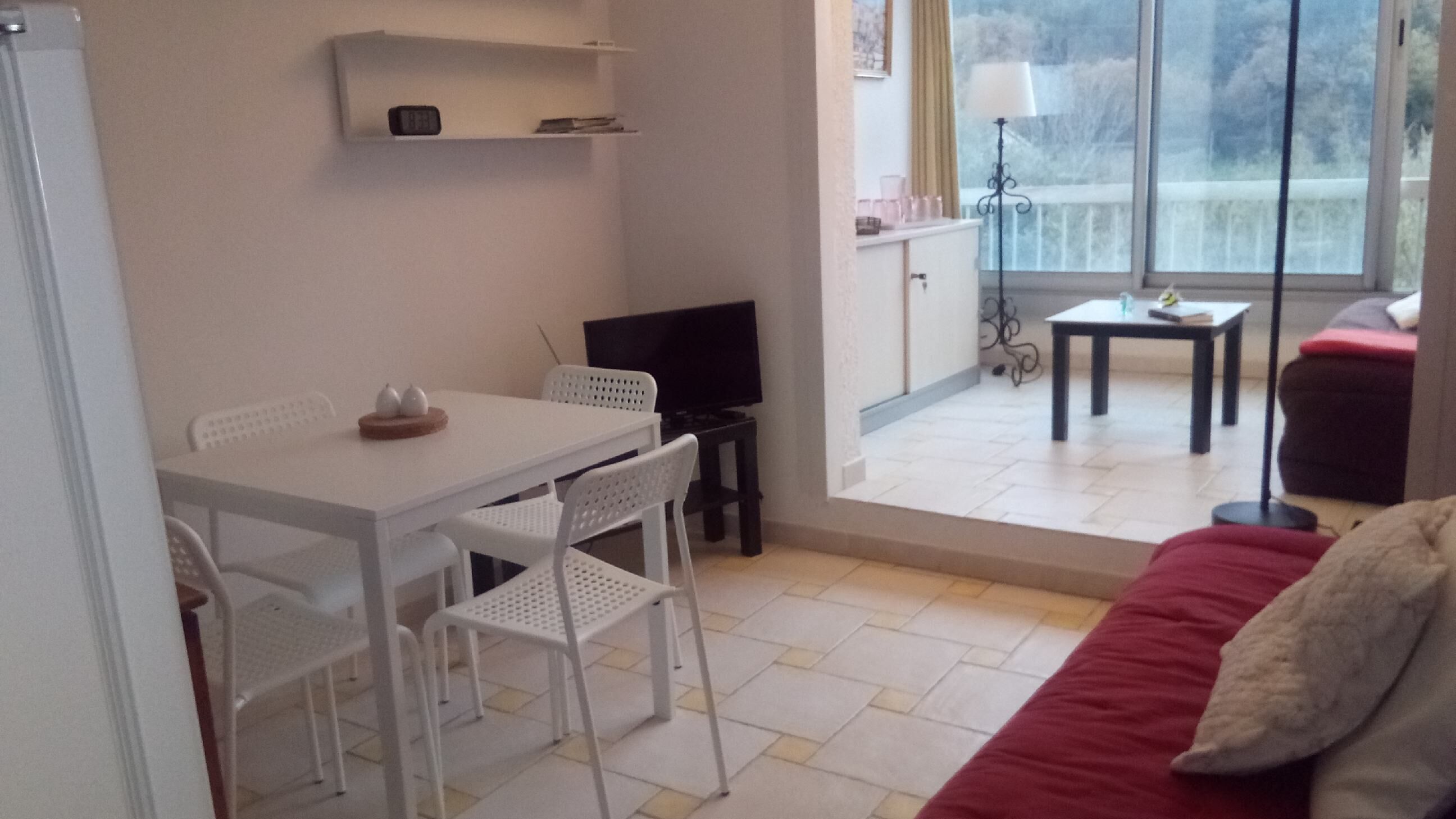 Ein kleiner, heller Raum mit einem weißen Tisch und Stühlen, einem Fernseher und einem Sofa.