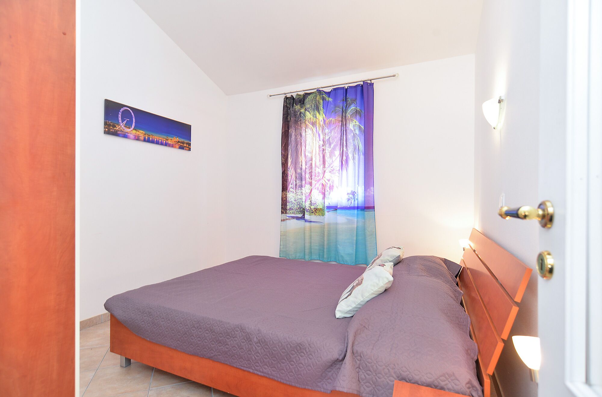Ein Schlafzimmer mit Bett, Tür, Wandbild und Vorhang mit tropischer Szene.