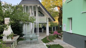Ein zweistöckiges Haus mit einer überdachten Terrasse und ein angrenzendes grünes Gebäude.
