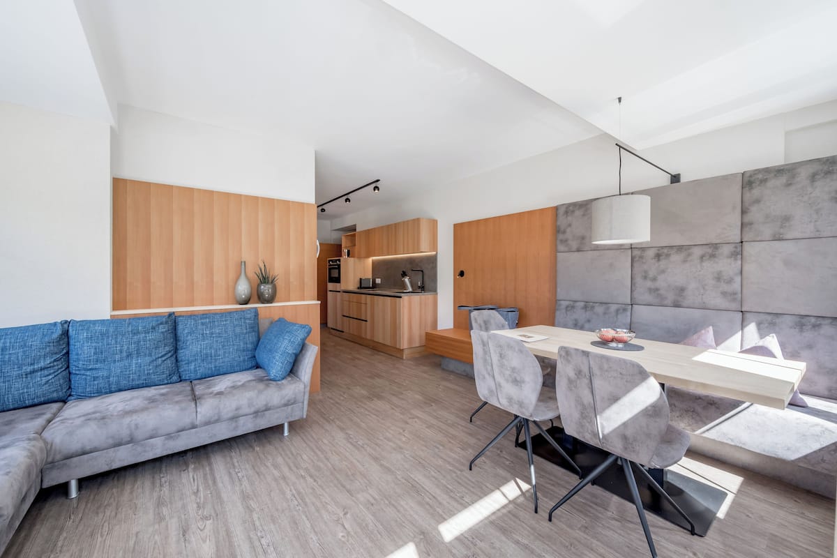Um espaço de estar moderno com sofá, mesa de jantar, cadeiras, cozinha e uma janela grande.