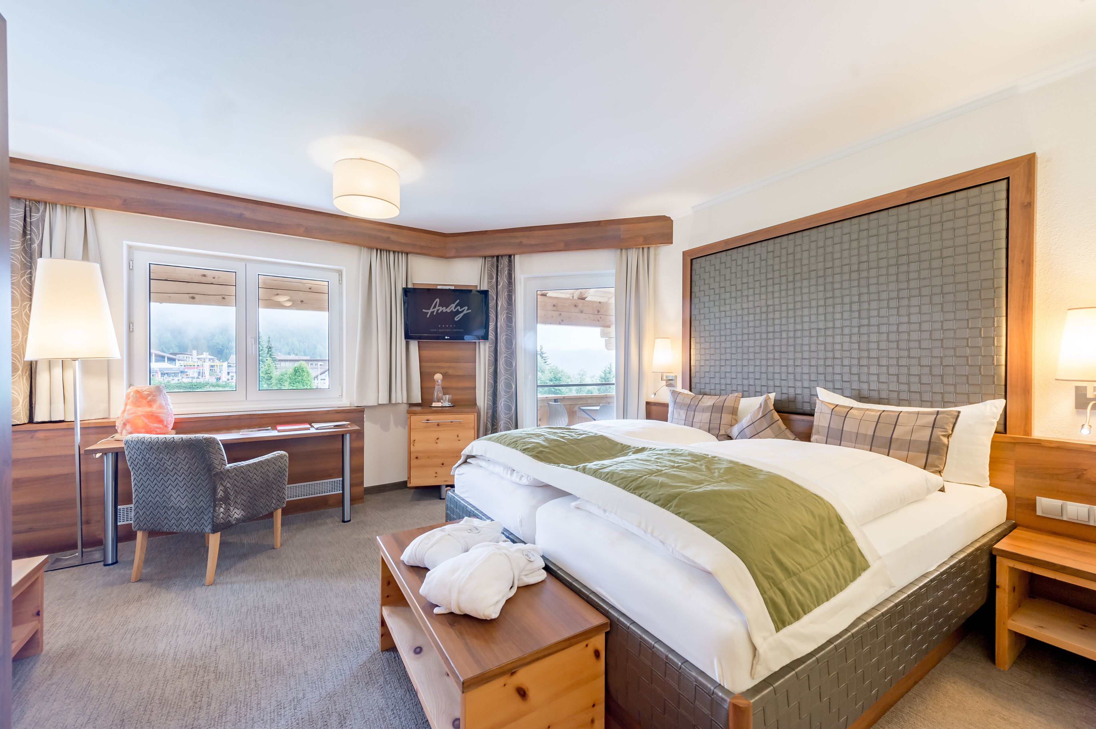 A hotel room with a large bed, a desk, a chair, a TV, and a view of the outdoors.