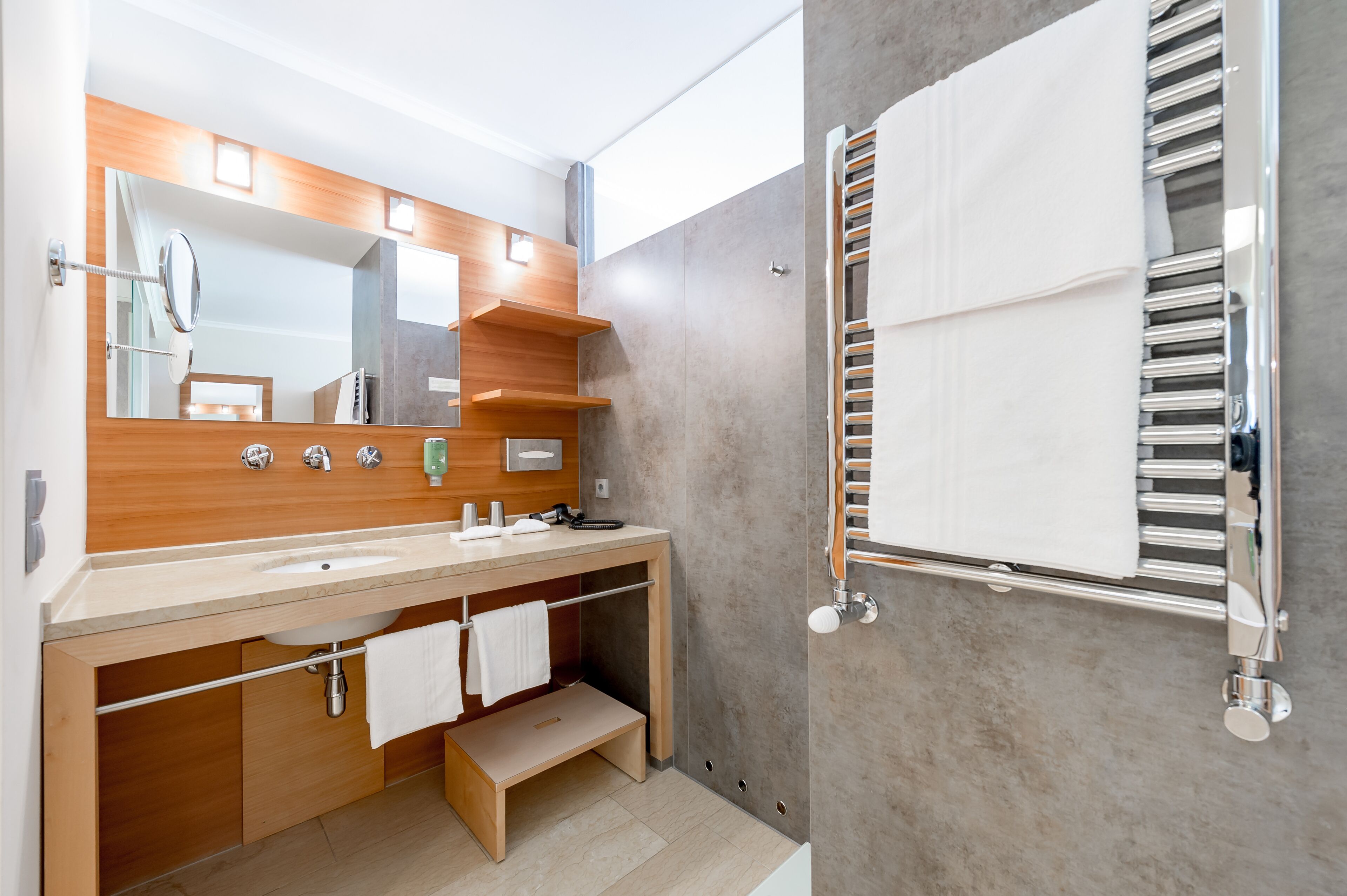 A modern bathroom with a wooden vanity, a large mirror, and a built-in towel rack.