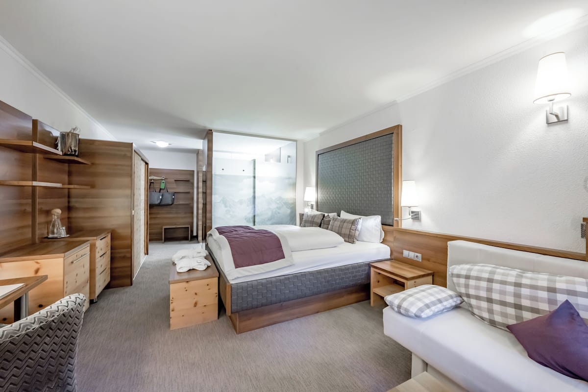 Quarto de hotel com cama, mesas de cabeceira, sofá, guarda-roupa e espelho.