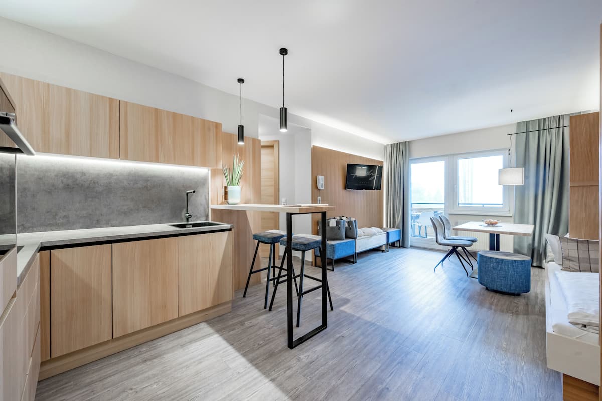Quarto de hotel moderno com cozinha compacta, área de refeições, televisão e uma janela grande.