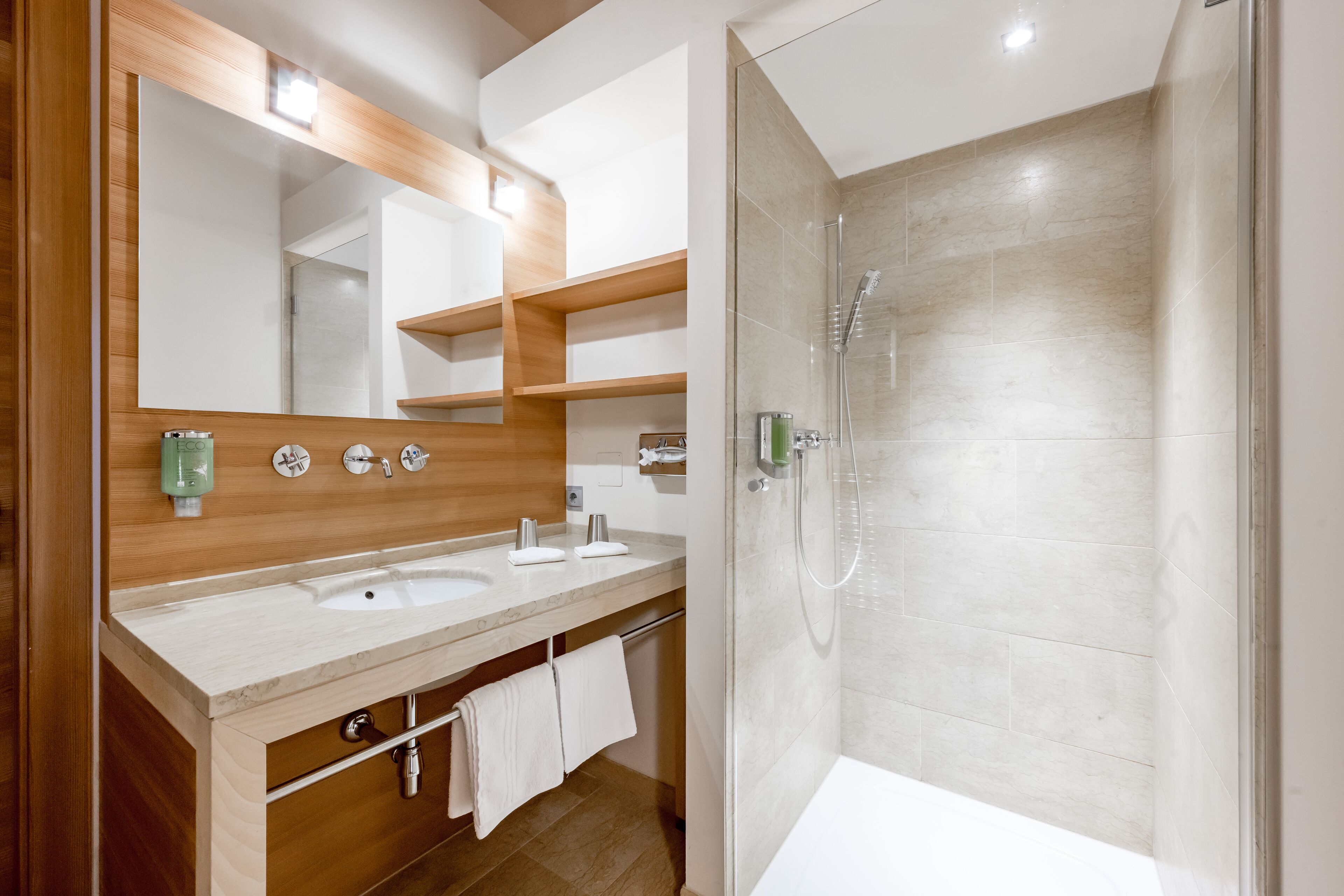 A modern bathroom with two sinks, a large mirror, and a glass-enclosed shower.