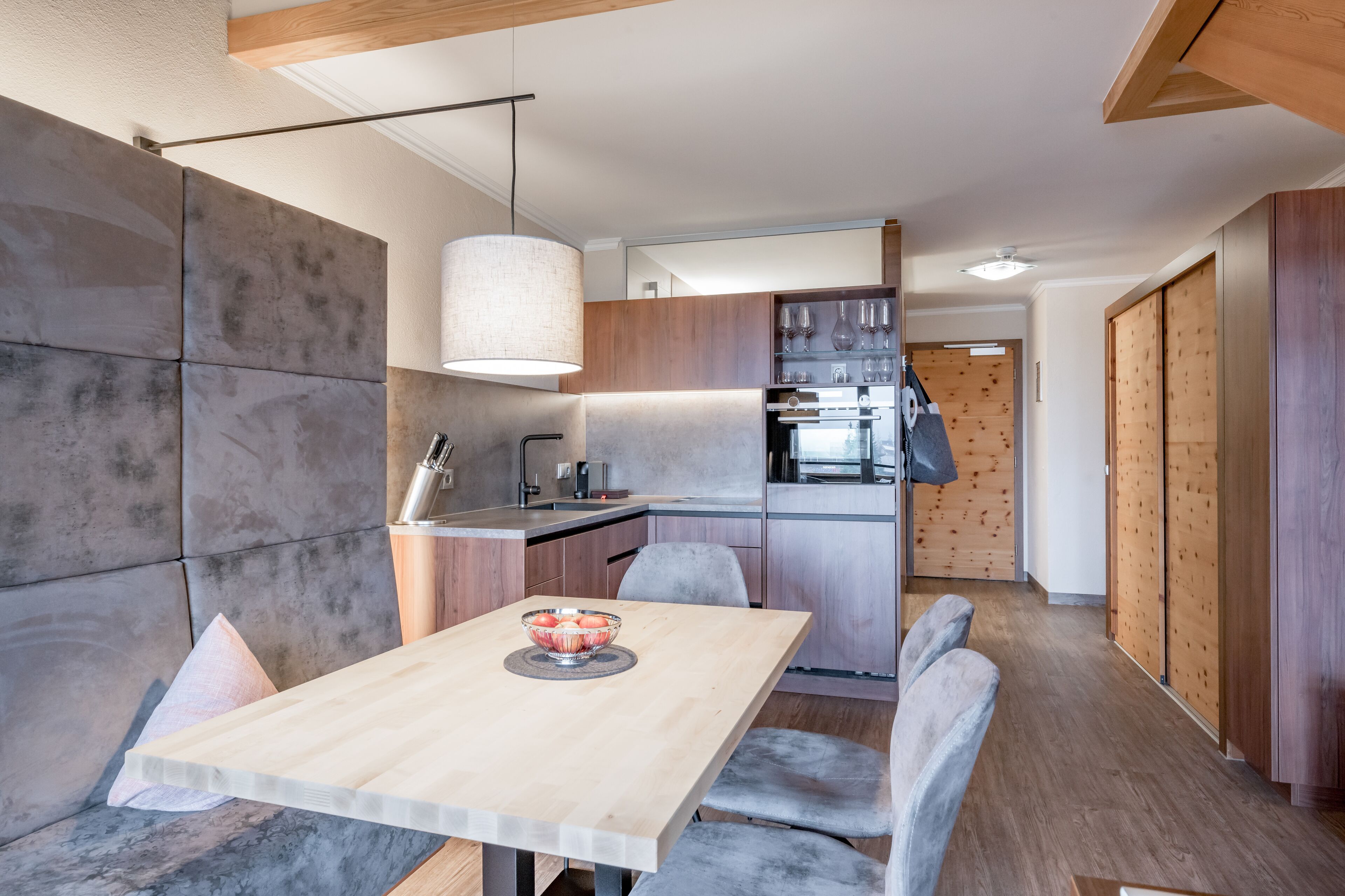 Eine moderne Küche mit Holztisch, grauen Stühlen und einer Pendelleuchte.