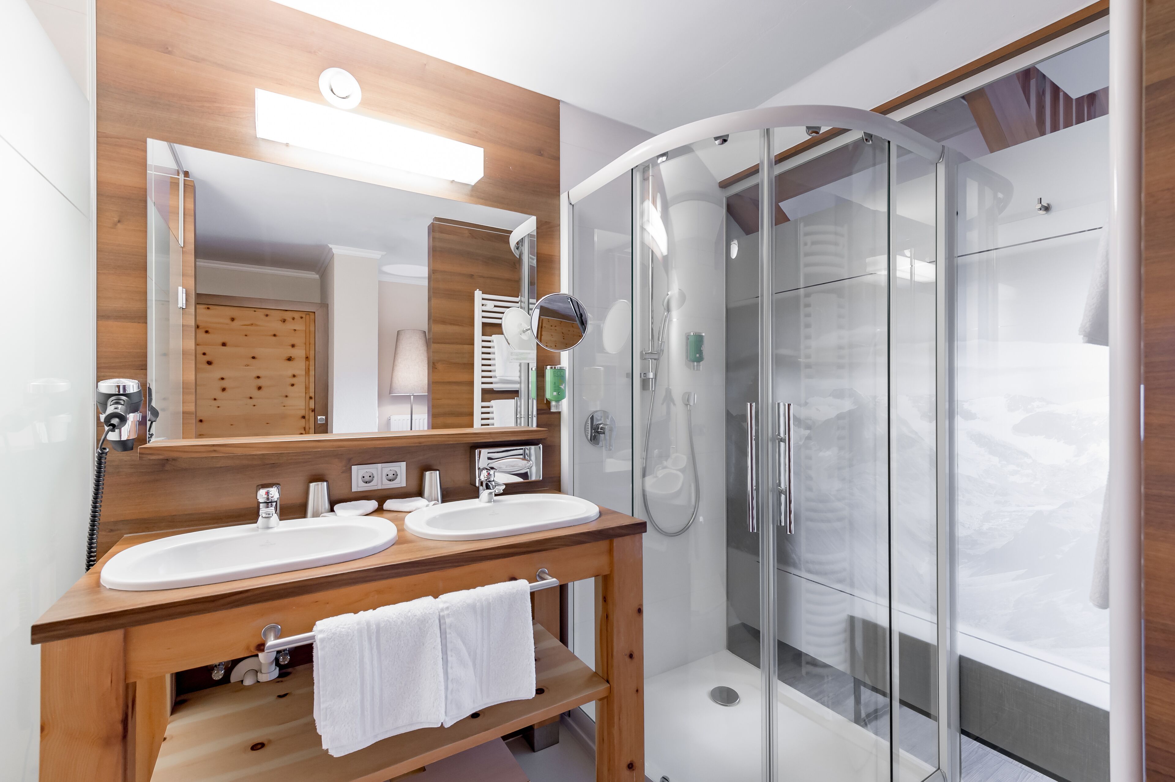 A modern bathroom with two sinks, a large mirror, and a glass-enclosed shower.