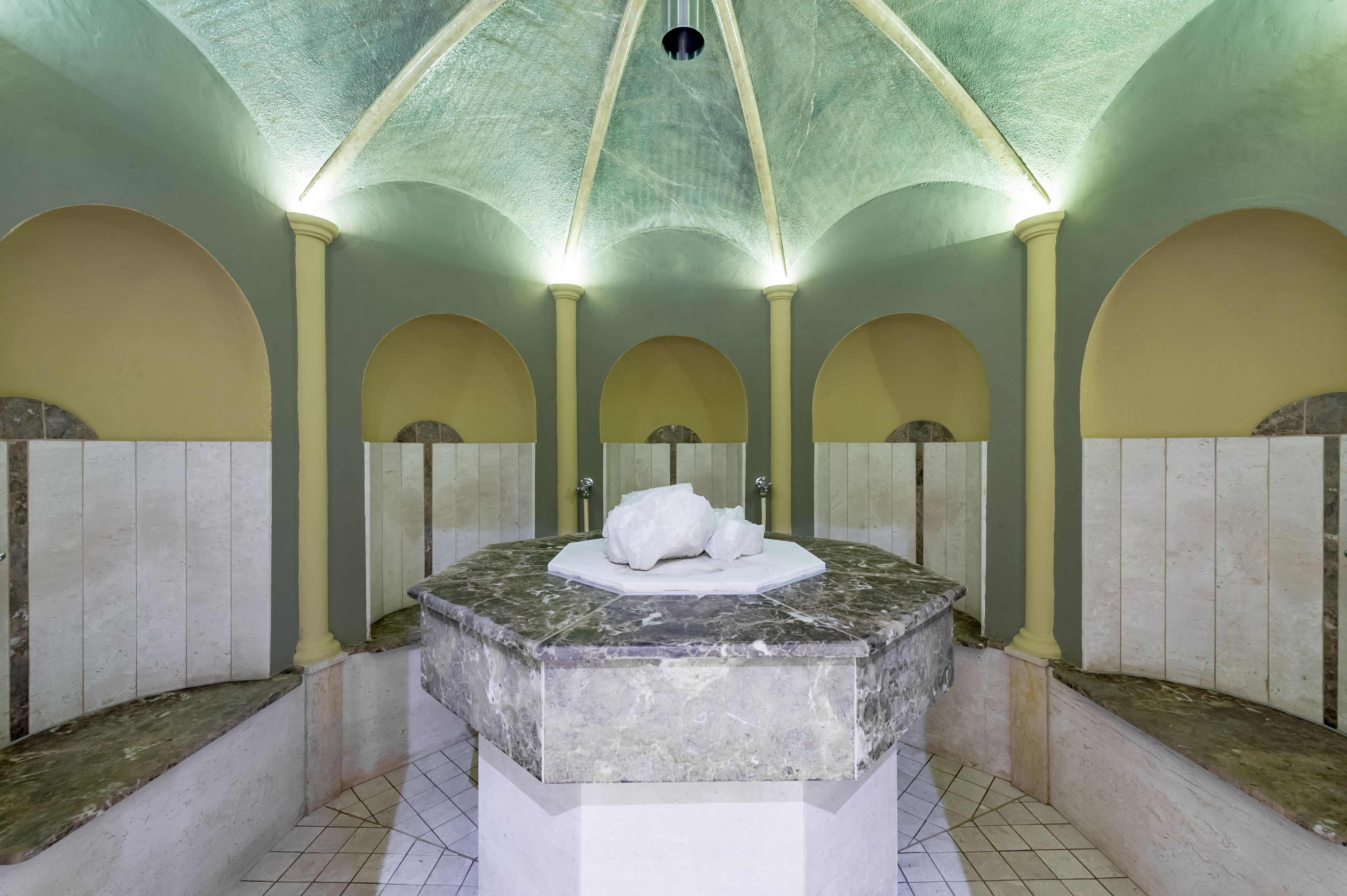 A public restroom with a central marble sink, tiled walls, and a vaulted ceiling.
