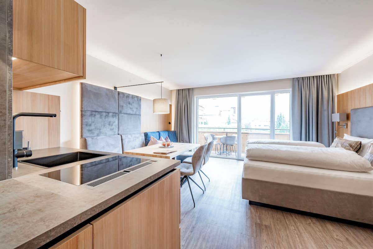 Quarto de hotel moderno com cozinha compacta, área de refeições, sofá e uma janela grande.