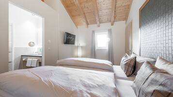 A bedroom with a wooden ceiling, a bed with white linens, a bedside table with a lamp, and a window with curtains.