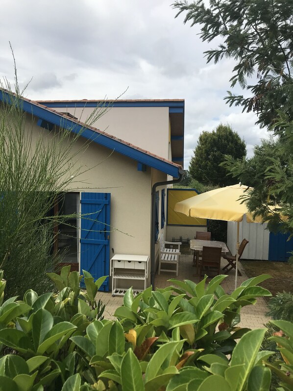 Una casa con puerta azul, un paraguas amarillo y una mesa con sillas afuera.