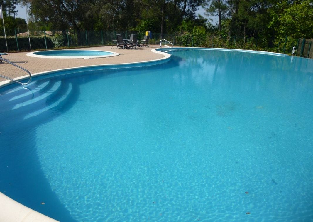 A clear blue swimming pool with a paved deck area and lounge chairs.