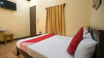 A neatly made bed with a red and white bedspread, a wooden nightstand with a telephone, and a wall-mounted TV.