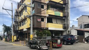 A multi-story building with balconies, a visible sign for a restaurant, and a parked car. - Rjat Guesthouse (Calamba)