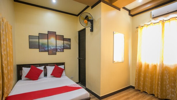 A hotel room with a bed, a wall-mounted air conditioner, a window with curtains, and a ceiling fan. - Rjat Guesthouse (Calamba)
