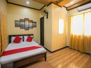 Una habitación de hotel con cama, aire acondicionado de pared, ventana con cortinas y ventilador de techo.