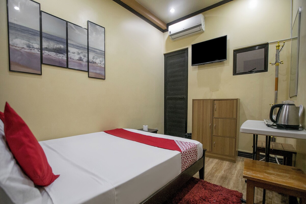 Una habitación de hotel con una cama, un escritorio con hervidor, televisor y armario.