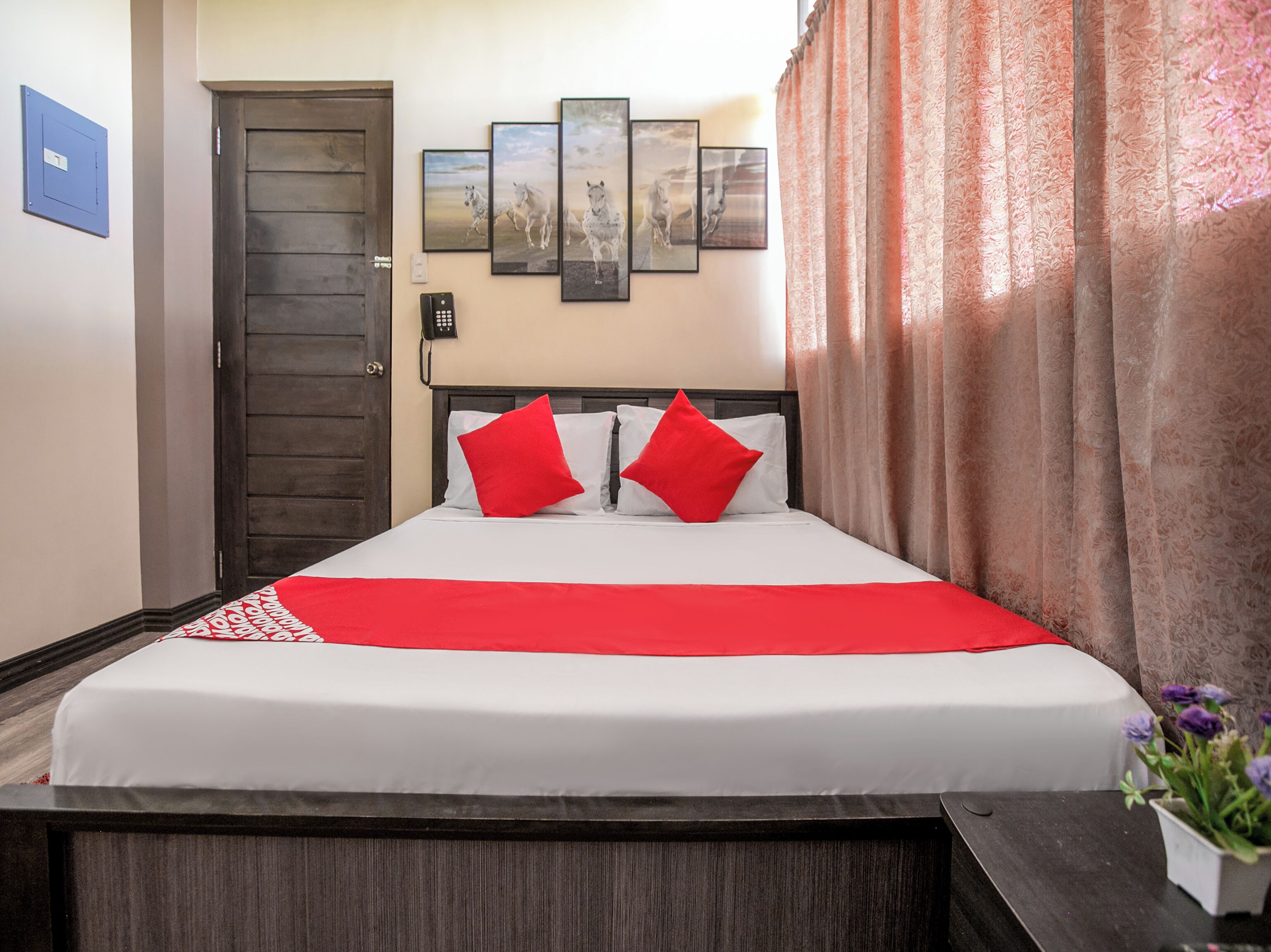 Ein Hotelzimmer mit Bett, Telefon, Tür und einer Wand mit gerahmten Bildern.