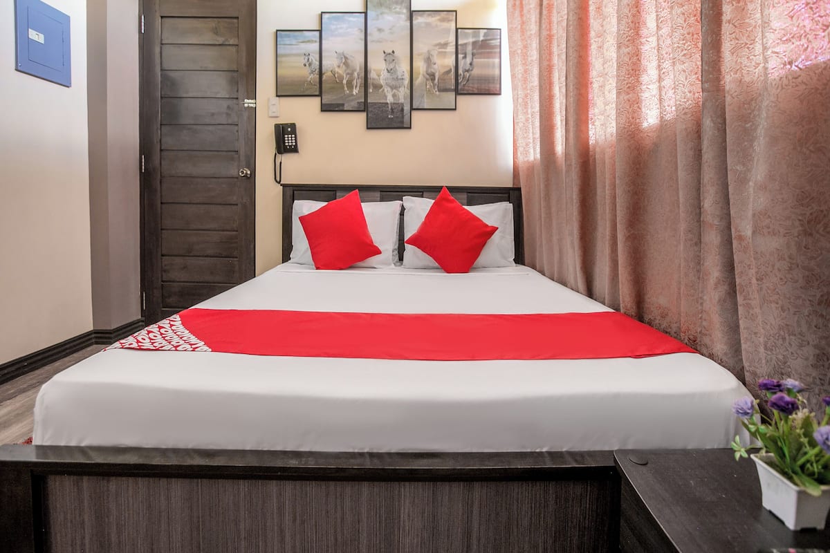 Habitación de hotel con cama, teléfono, puerta y pared decorada con cuadros.