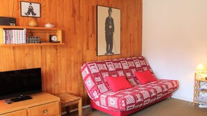 Una habitación acogedora con una pared de madera, un sofá rojo estampado, un televisor y una pequeña mesa de madera.
