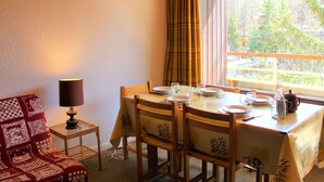 Un comedor con una mesa dispuesta para cuatro, una lámpara y vistas a un bosque a través de una ventana.