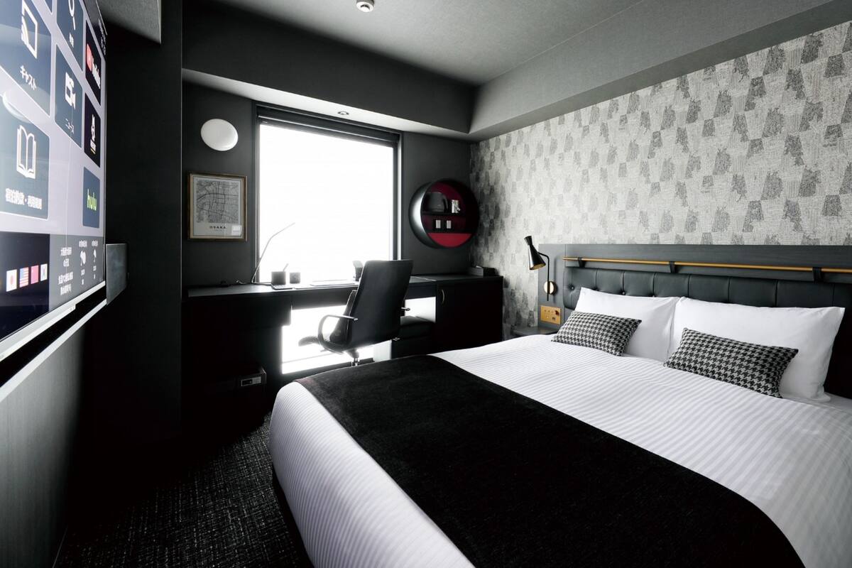 Ein modernes Hotelzimmer mit einem großen Bett, einem Schreibtisch mit Stuhl, einem Computer und einem Fenster mit Ausblick.
