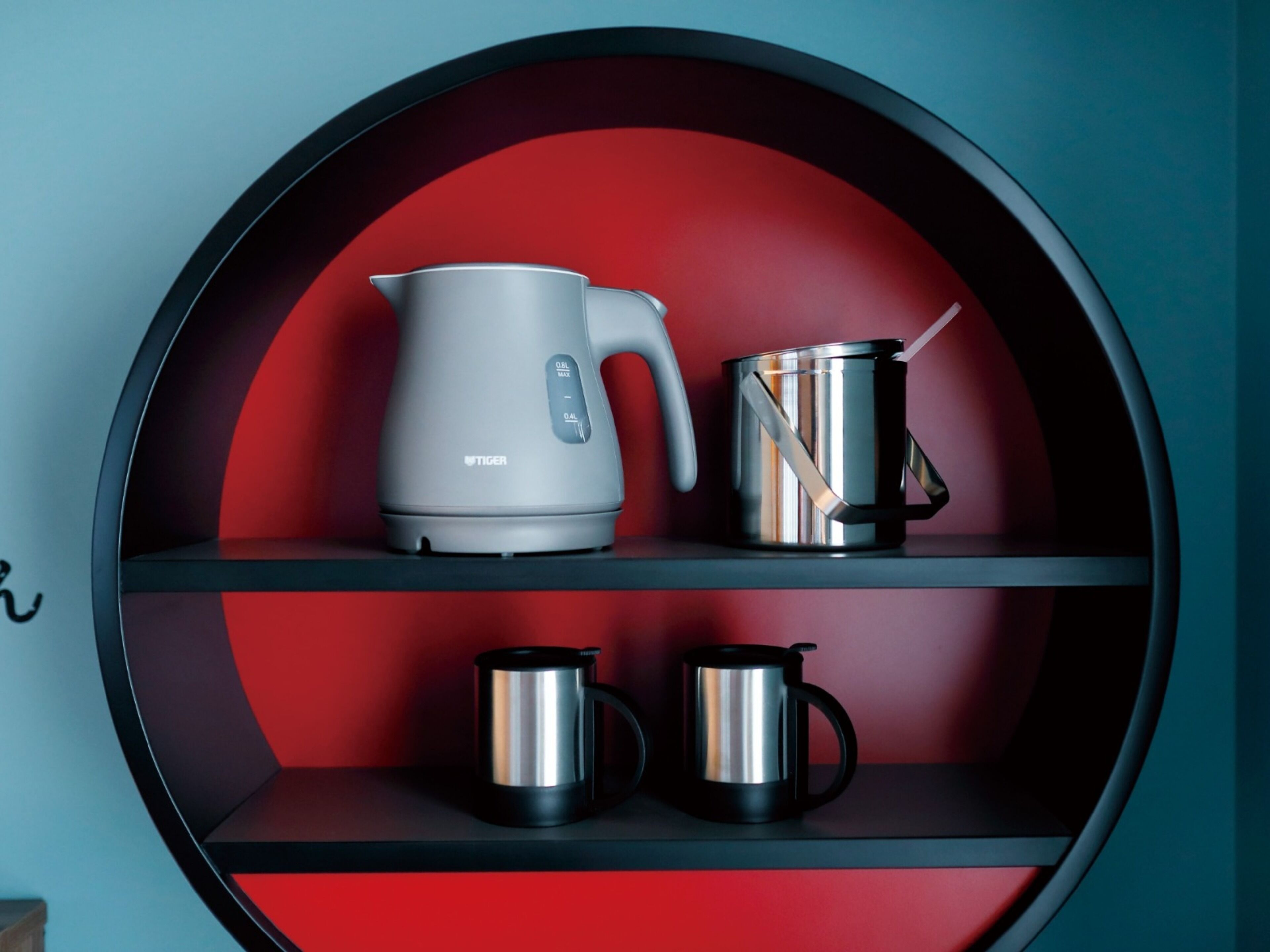 Una estantería circular con interior rojo, que sostiene una tetera, una olla y dos tazas.