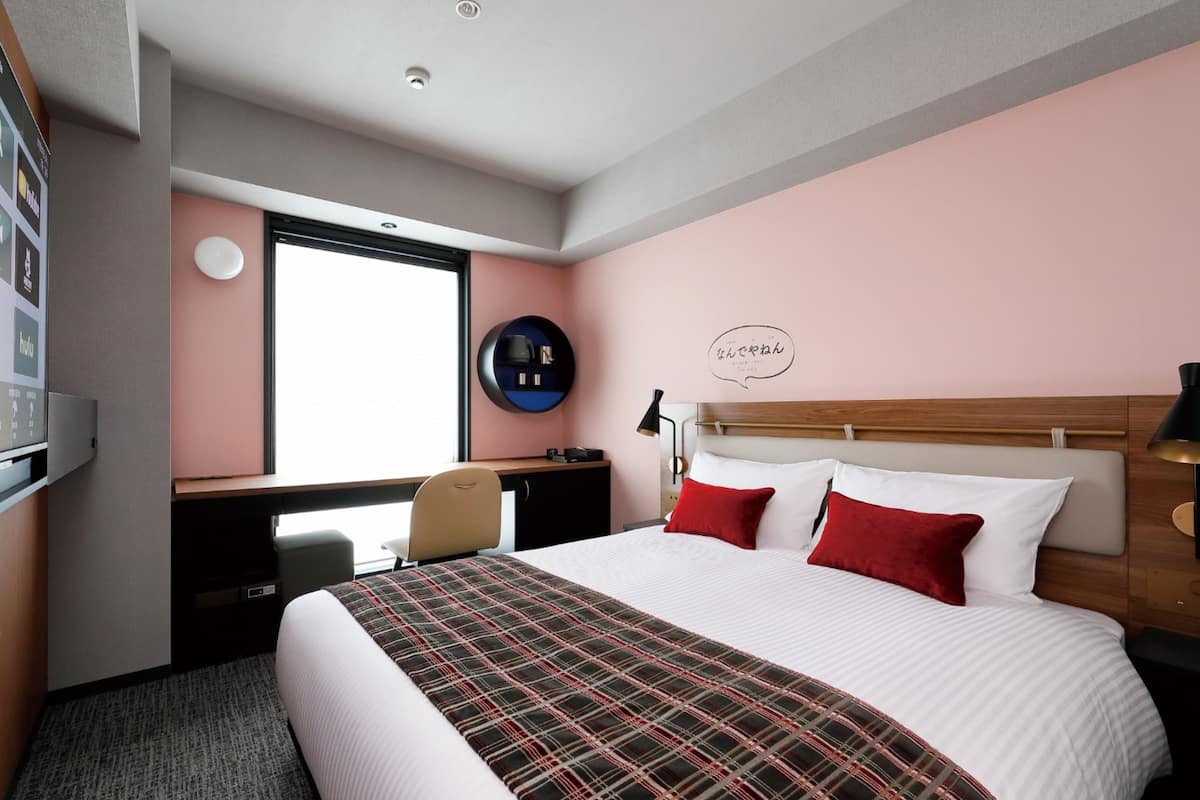 Ein Hotelzimmer mit einem großen Bett, einem Schreibtisch mit Stuhl, einer runden Wanddekoration und einem Fenster.