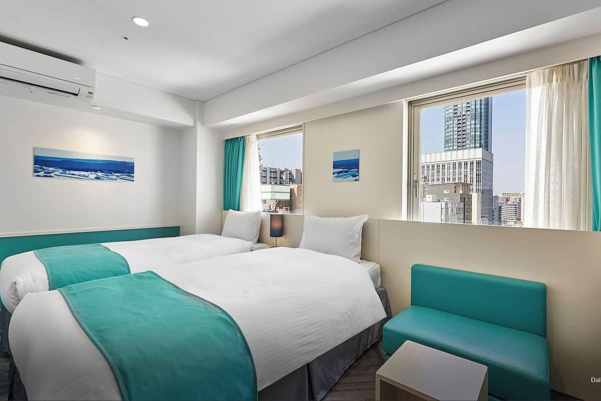 Ein Hotelzimmer mit zwei Betten, einer Sitzecke und großen Fenstern mit Blick auf die Stadt.