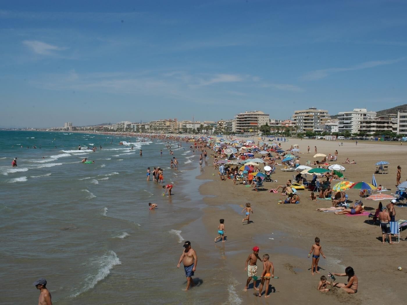 A crowded beach with people sunbathing and swimming.
