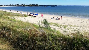A beach with people relaxing and sunbathing, a sandy shore, and a clear blue sky.
