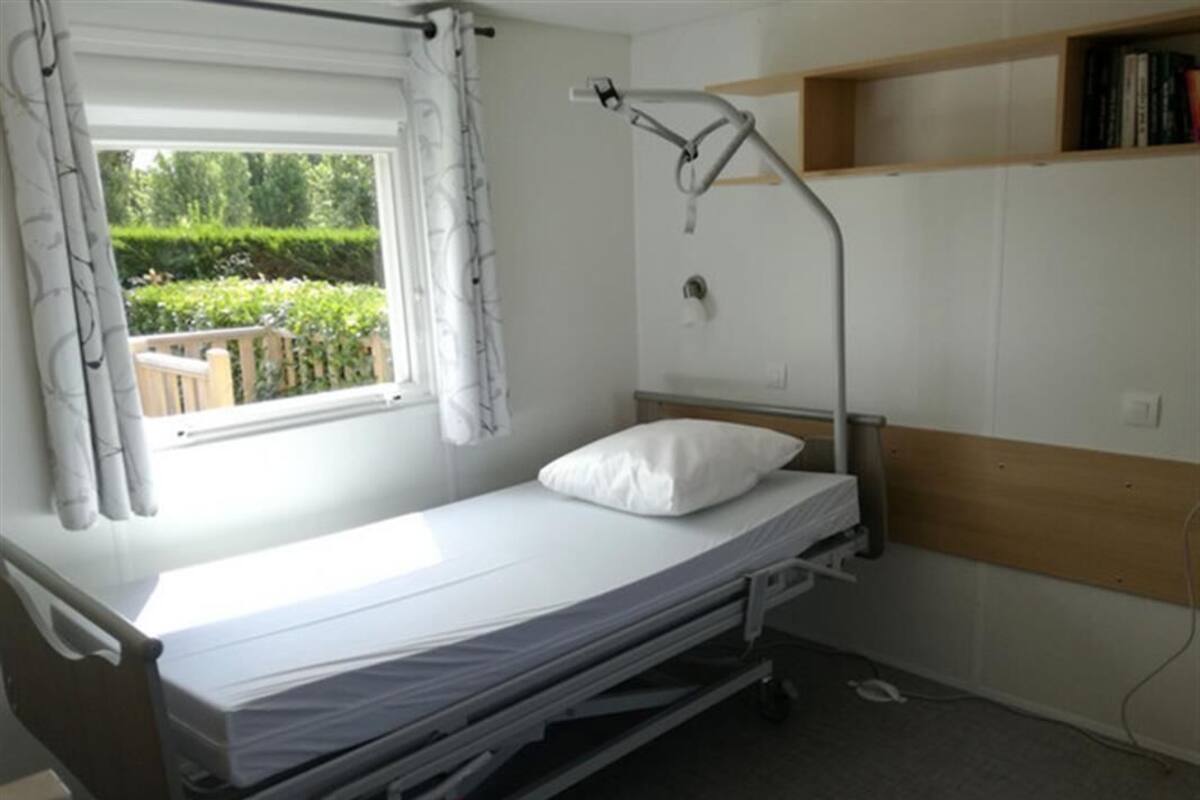 Une chambre avec un lit simple, une fenêtre, une table de chevet et une étagère au-dessus du lit.