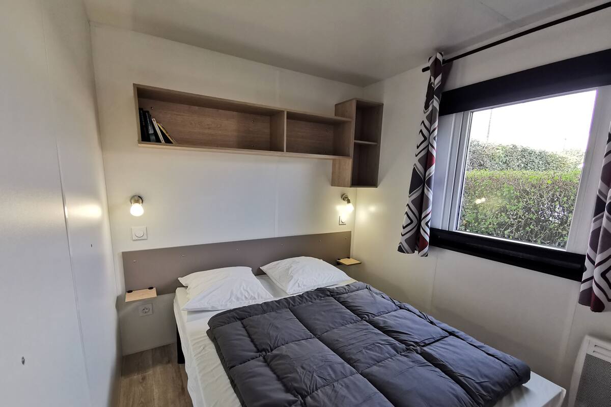 Une chambre à coucher comprenant un lit, des tables de chevet, des étagères intégrées et une fenêtre avec des rideaux.