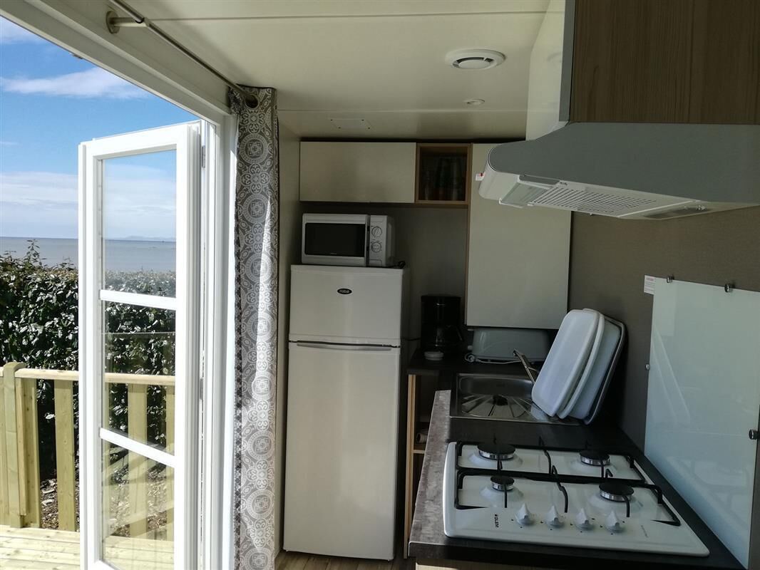 Una kitchenette compacta con estufa a gas, microondas y refrigerador, una ventana pequeña y vistas al exterior.