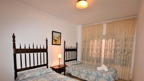 A room with two beds, each with floral bedding, a nightstand with a lamp, and a framed picture on the wall. - Apartament Suiza - Calafell (Calafell)